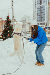 A beautiful young girl throws snow and plays with her white dog in winter, Festive New Year's mood, happy woman with a dog