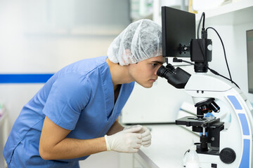 Focused young veterinarian deeply engrossed in examining samples under microscope in veterinary office, seeking to identify health issues in pet and provide accurate diagnoses for effective treatment