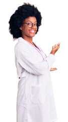 Young african american woman wearing doctor coat and stethoscope inviting to enter smiling natural...