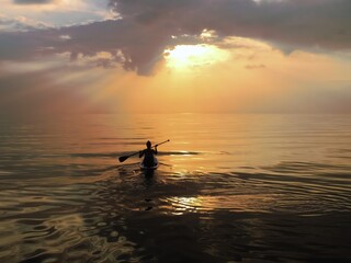 Fototapeta premium silhouette of a girl on a boat with an oar on the sea, in a calm, with a small surf, against the backdrop of dark clouds in the evening, before sunset