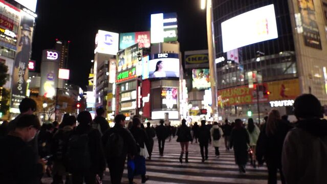 SHIBUYA, TOKYO, JAPAN - OCT 2023 : Back shot of crowd of people and cityscape around Shibuya Crossing at night. Japanese people, travel and tourism concept video. Slow motion walking view shot.