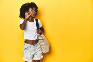 Young girl with beach bag ready for holiday, yellow backdrop trying to listening a gossip.