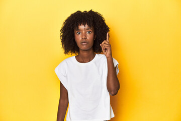 Teen girl in white tank top, yellow studio background having an idea, inspiration concept.