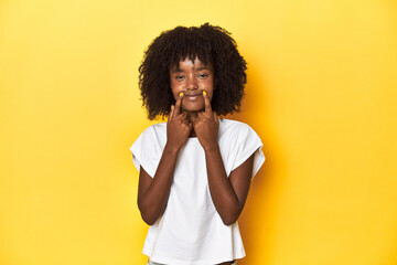 Teen girl in white tank top, yellow studio background doubting between two options.