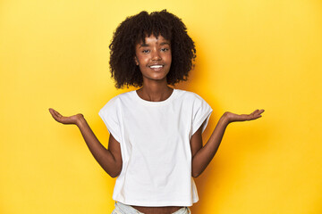 Teen girl in white tank top, yellow studio background makes scale with arms, feels happy and...