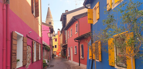 Street of the city of Caorle with colorful houses against the backdrop of the Bell Tower of the Cathedral. Panorama. - obrazy, fototapety, plakaty