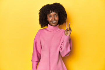 Obraz na płótnie Canvas Teen girl in pink sweatshirt, yellow studio backdrop joyful and carefree showing a peace symbol with fingers.
