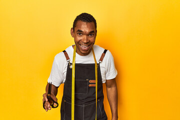 African American tailor with tools, yellow studio, laughing and having fun.