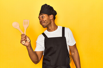 African American cook holding wooden spoon and fork in a yellow studio
