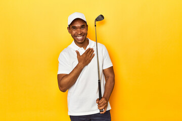 African American man golfer, yellow studio backdrop, laughs out loudly keeping hand on chest.