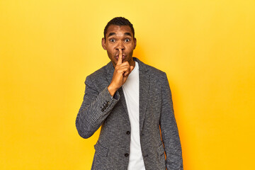 African American man in casual blazer, yellow studio, keeping a secret or asking for silence.