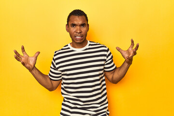 African American man in striped t-shirt, yellow studio, screaming with rage.