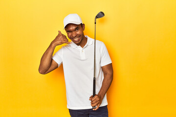 African American man golfer, yellow studio backdrop, showing a mobile phone call gesture with...