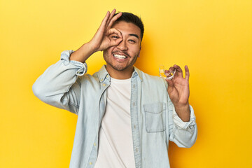 Asian man with invisible dental corrector, yellow studio backdrop excited keeping ok gesture on eye.