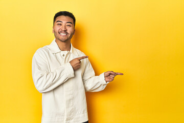 Asian man in crisp white shirt on yellow studio excited pointing with forefingers away.
