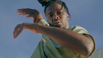 Modern dancer looking camera sky background. African american guy moving hands