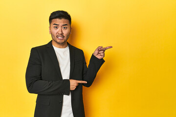 Asian man in black business jacket on yellow studio shocked pointing with index fingers to a copy...