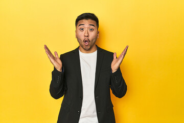 Asian man in black business jacket on yellow studio surprised and shocked.