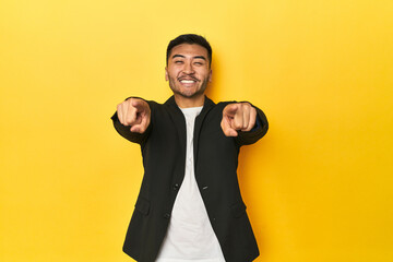 Asian man in black business jacket on yellow studio cheerful smiles pointing to front.