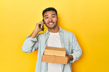 Asian man holding a food delivery and talking on the phone on a yellow background.