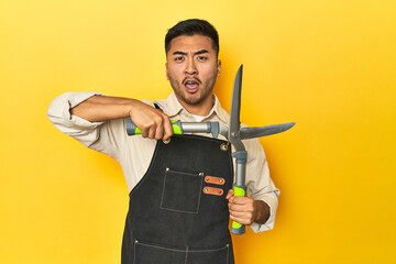 Asian gardener holding pruning shears against a yellow studio background.