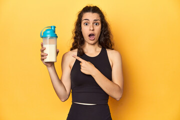 Woman holding a protein shake, in sportswear, pointing to the side
