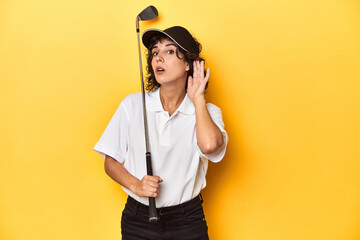 Athletic Caucasian woman with curly hair golfing in studio trying to listening a gossip.
