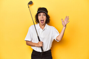 Athletic Caucasian woman with curly hair golfing in studio receiving a pleasant surprise, excited...