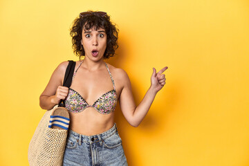 Caucasian woman in bikini with beach bag, studio pointing to the side