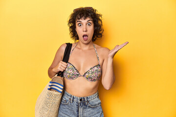 Caucasian woman in bikini with beach bag, studio surprised and shocked.