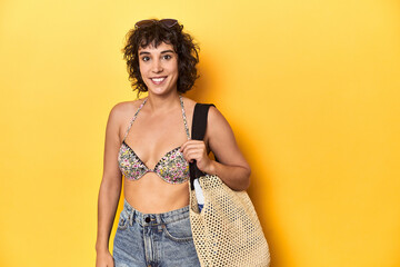 Summer ready woman with beach gear and plane ticket, yellow studio backdrop.