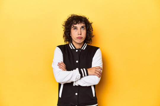 Curly-haired Caucasian woman in baseball jacket tired of a repetitive task.