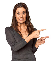 Elegant middle-aged Caucasian woman in studio setting shocked pointing with index fingers to a copy...