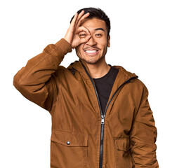 Young Chinese man in studio background excited keeping ok gesture on eye.