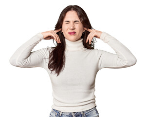Fototapeta premium Young Caucasian woman in a studio setting covering ears with fingers, stressed and desperate by a loudly ambient.