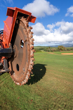 A giant rockwheel, drum of a trench digging machine, earth saw for irrigation and cable laying project on the green grass of a golf curse, Kauai, Hawaii