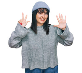 Young hispanic woman wearing cute wool cap showing and pointing up with fingers number eight while smiling confident and happy.