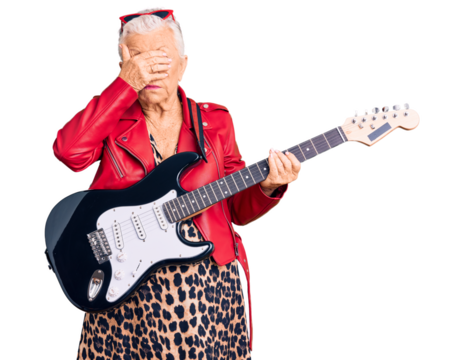 Senior beautiful woman with blue eyes and grey hair wearing a modern look playing electric guitar covering eyes with hand, looking serious and sad. sightless, hiding and rejection concept