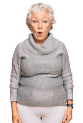 Senior grey-haired woman wearing casual winter sweater in shock face, looking skeptical and...