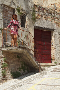 A young woman with graceful curves confidently poses on the ruins of an ancient external staircase, immersing herself in the evocative atmosphere of a village in southern Italy.