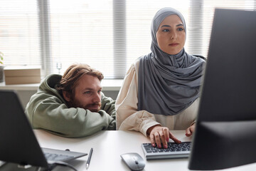 Front view at two people in IT development team working on computer together with Muslim young...