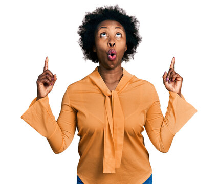 African american woman with afro hair wearing elegant shirt amazed and surprised looking up and pointing with fingers and raised arms.