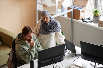 High angle portrait of Muslim young woman looking at computer screen with male colleague in office