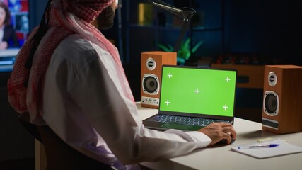 Arabic man scrolling on mockup laptop while working from home. Self employed person writing emails...