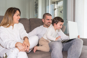 Family using laptop with a baby sitting on the sofa