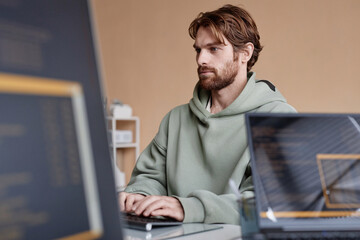 Side view portrait of young bearded computer programmer writing code at workplace in office