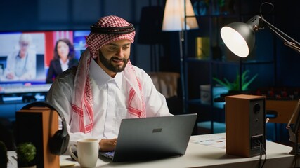 Arab businessman typing on laptop, surfing the net while drinking cup of coffee. Middle Eastern man conversing through email, solving clients tasks while enjoying hot beverage - obrazy, fototapety, plakaty