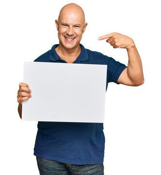 Middle age bald man holding blank empty banner pointing finger to one self smiling happy and proud
