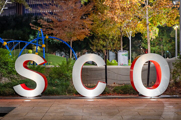 Red and gray three-dimensional 3d letters SCO with an evening outdoor background.
