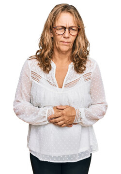 Middle age blonde woman wearing casual white shirt and glasses with hand on stomach because indigestion, painful illness feeling unwell. ache concept.